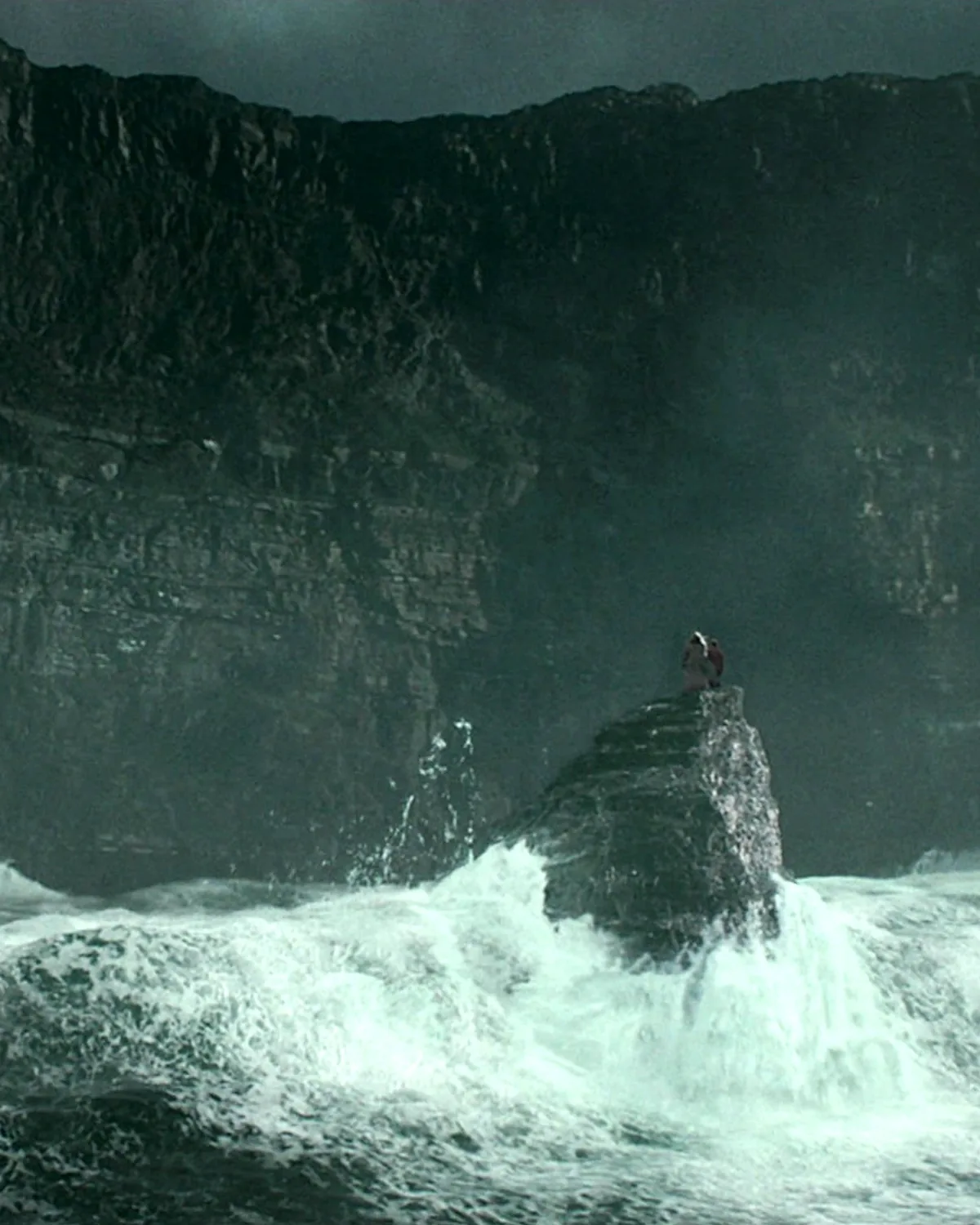 Waves breaking against a sea cave beneath black cliffs
